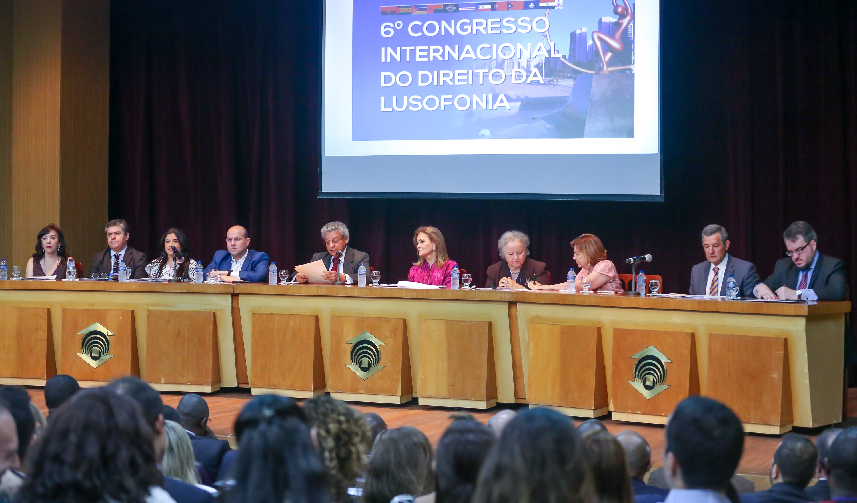 mesa no palco de um auditório com várias pessoas sentadas